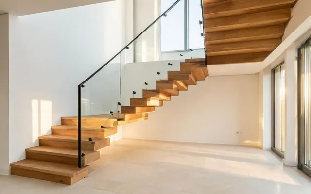 Escalier intérieur sur mesure en bois massif avec garde-corps acier noir et panneaux de verre dans une maison lumineuse à Sion
