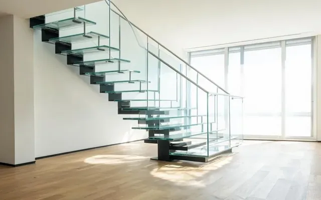 Escalier contemporain à marches en verre feuilleté transparent avec structure en acier noir et garde-corps en verre dans un séjour lumineux